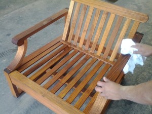 a man refinishing a wooden teak lawn chair with a cloth