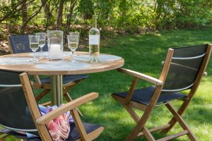 A teak outdoor table and chairs set with a bottle of wine and wine glasses sitting on top of it