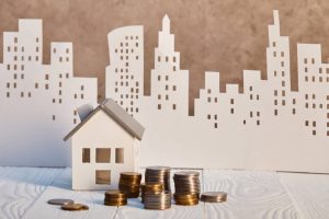 A miniature of a house next to a pile of coins, representing the housing market