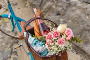 Flowers and a bottle of champagne packed in a bicycle basket on the beach