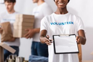 Woman wearing a volunteer shirt holding up a clip board; other volunteers are in the background
